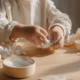 Kleine kinderhanden met een beetje witte verf erop bezig met knutselwerk aan een lichte houten tafel in ochtendlicht