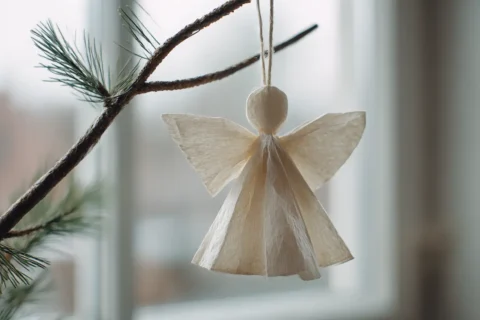 Close up van een eenvoudig zelfgemaakt papieren ornament hangend aan een dennentak in zacht daglicht