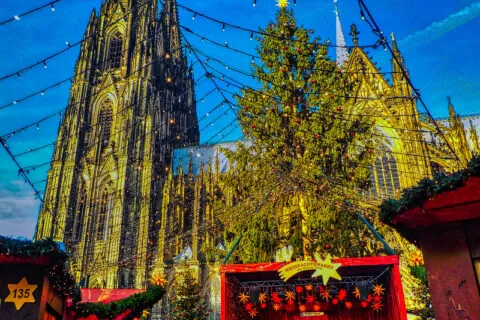 Kerstmarkt aan de Kölner Dom met verlichte kerstbomen en kraampjes in de avond