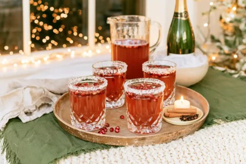 Houten dienblad met vier glazen cranberrycocktail, kan en fles cava op een tafel met kaarslicht