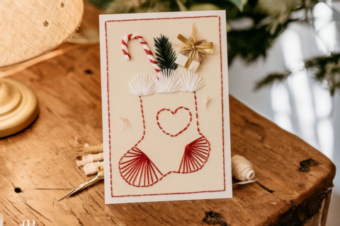 Handgemaakte kerstkaart met een geborduurde kerstsok in rood en wit garen met cadeautje en dennentakje