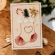 Handgemaakte kerstkaart met een geborduurde kerstsok in rood en wit garen met cadeautje en dennentakje