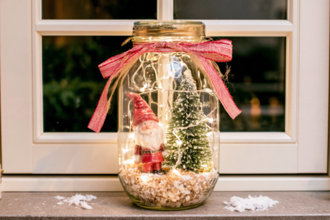 Glazen weckpot met kunstsneeuw een rode kerstkabouter klein boompje en brandend lichtsnoer met rode strik