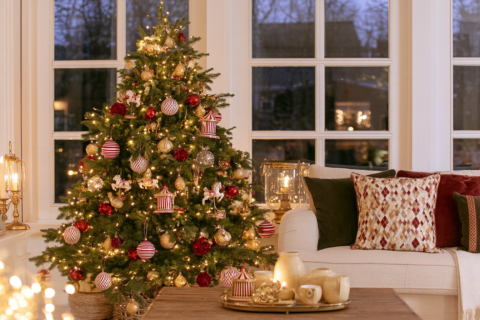 Kerstboom met gestreepte ornamenten, carrouselpaardjes en harlekijnkussen in een warme woonkamer