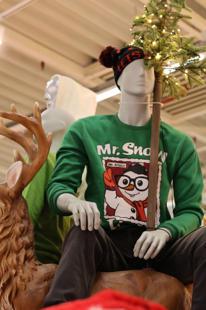 Etalagepop met een groene kersttrui met sneeuwpop naast een rendier